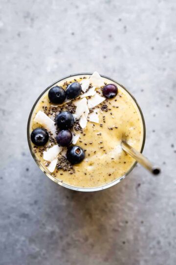 mango banana smoothie in a cup with a straw and blueberries on top