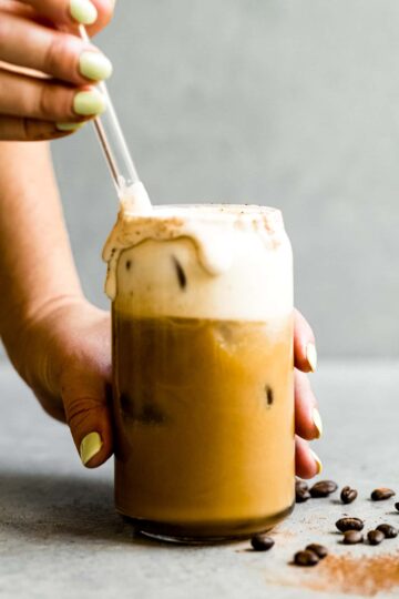 stirring irish cream coffee in a glass cup with a glass straw